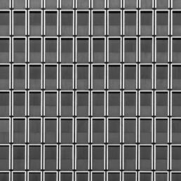 Black and white photo of a building façade with a grid of repetitive rectangular window frames, resembling a minimalist cityscape.