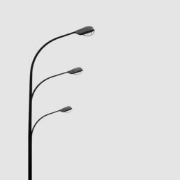 Three curved street lamps aligned vertically against a pale gray sky, each extending from the same pole at different heights, resembling a minimalist trio in motion.