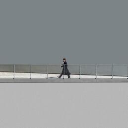 A person dressed in black walks on a fenced-overpass against a flat grey wall and background, evoking a minimalist and isolated cityscape.
