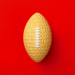 A beige cracker designed to look like an American football with white laces, placed on a bright red background.