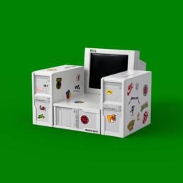 Armchair designed from vintage white computer towers and a CRT monitor, decorated with 90s band and brand stickers, placed against a green background.
