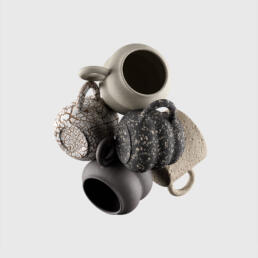 A cluster of five uniquely textured ceramic mugs in varying earthy tones, suspended against a neutral background.